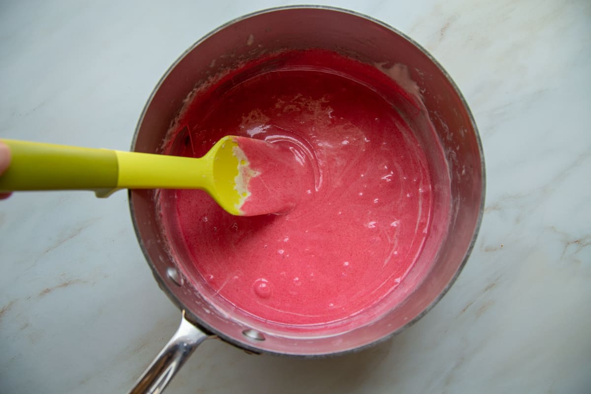 red marshmallow mixture in a saucepan with a yellow spatula.