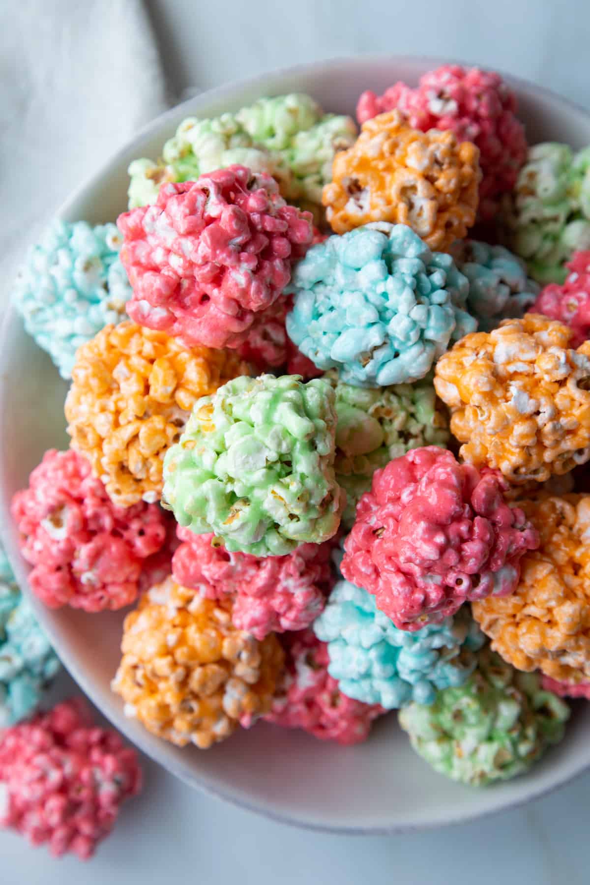 a pile of red, green, orange, and blue popcorn balls in a white dish.