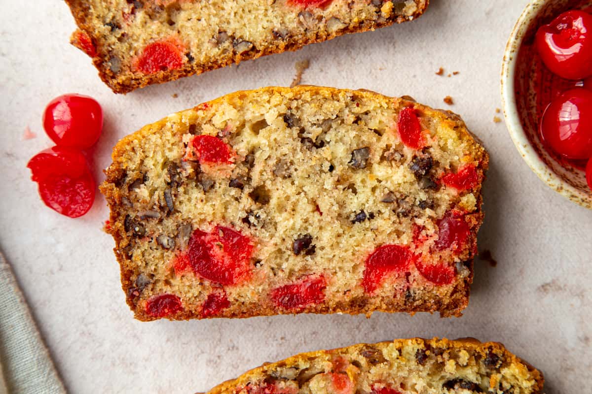 slice of quick bread with cherries and pecans next to a few maraschino cherries.