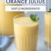 orange julius in two decorative glasses and also in a glass pitcher, next to a blue tea towel.