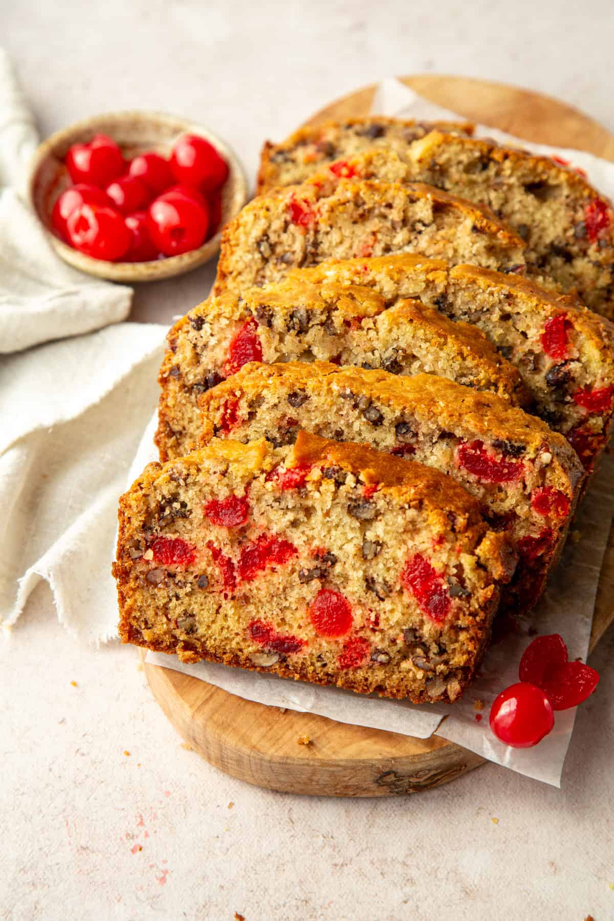 slices of cherry bread on a wooden serving platter next to a bowl of maraschino cherries.