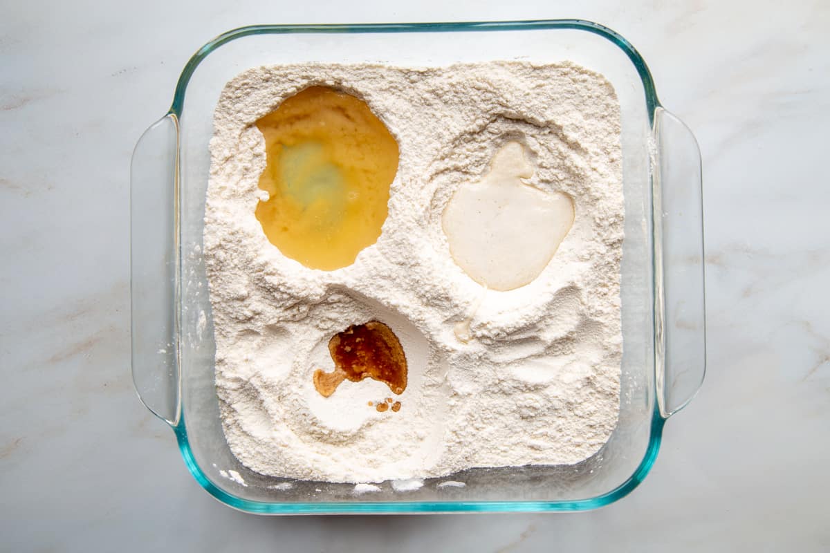 dry ingredients in a square glass dish, with three wells filled with oil, vinegar, and vanilla.