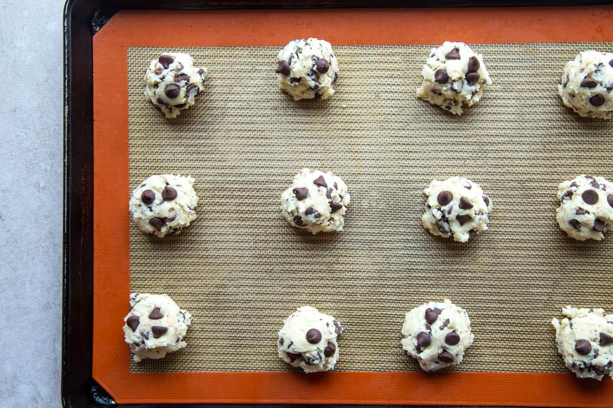 uncooked chocolate chip cookie dough on a silicone mat on a baking sheet.