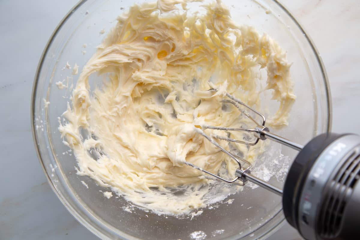 vanilla frosting in a glass bowl with a hand mixer.