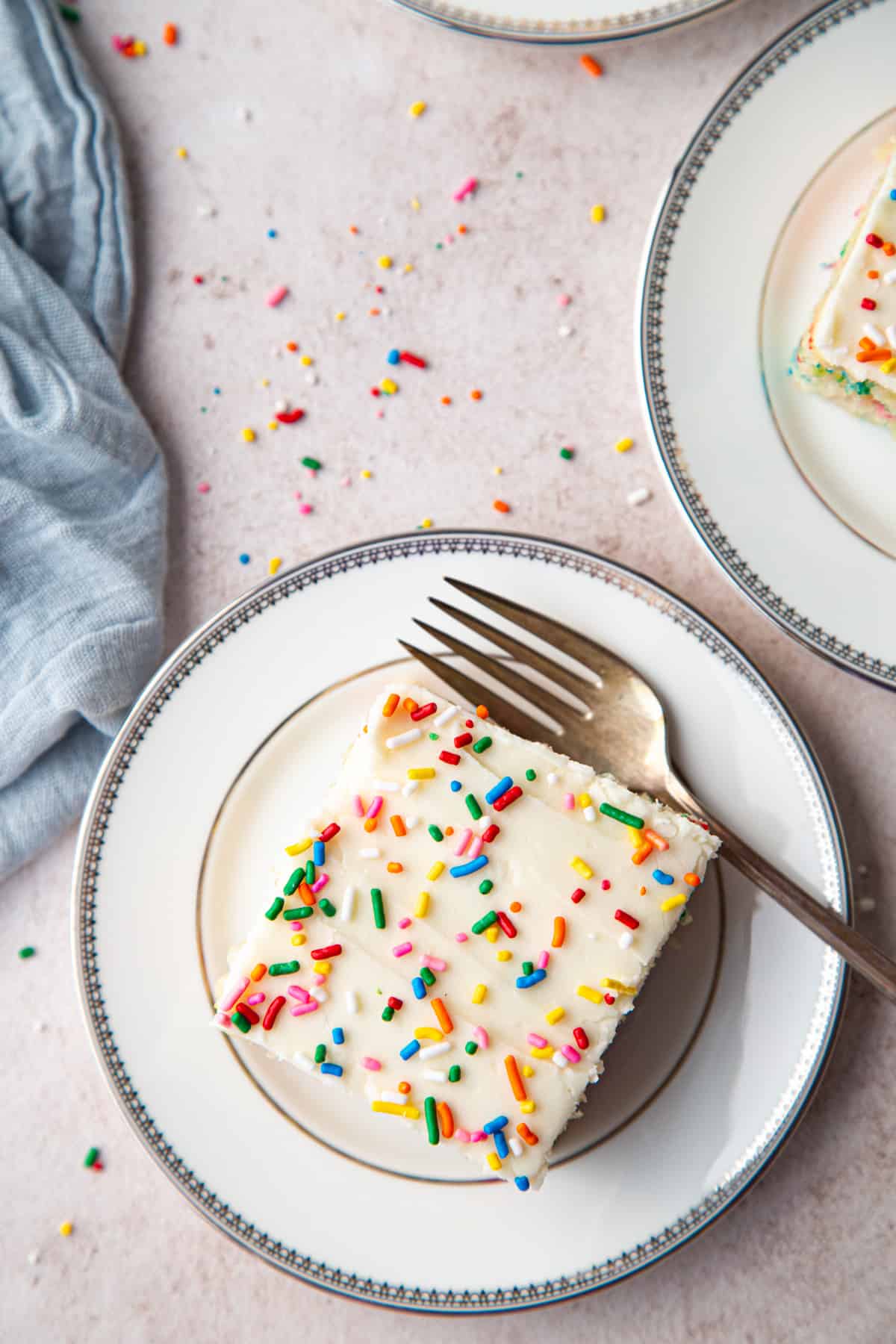 slice of wacky cake topped with frosting and sprinkles on a white and silver plate on a pink background.