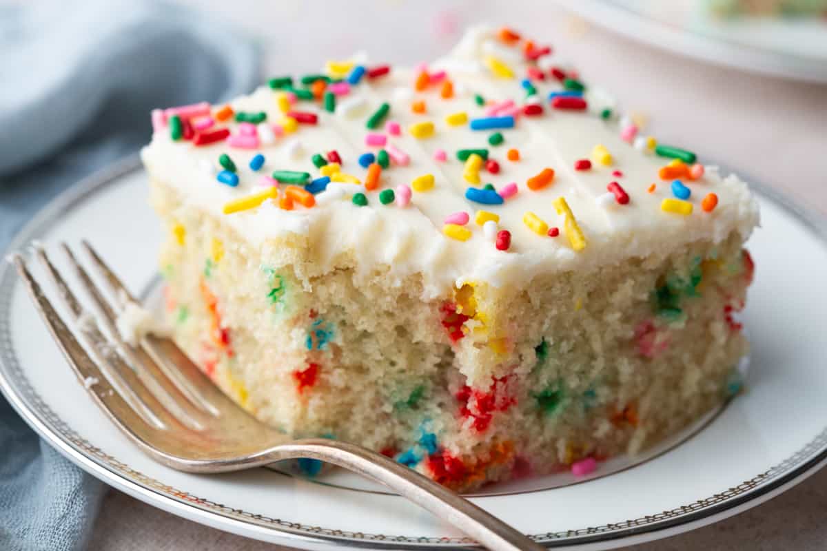 slice of vanilla wacky cake with a bite taken out, topped with vanilla frosting and sprinkles.