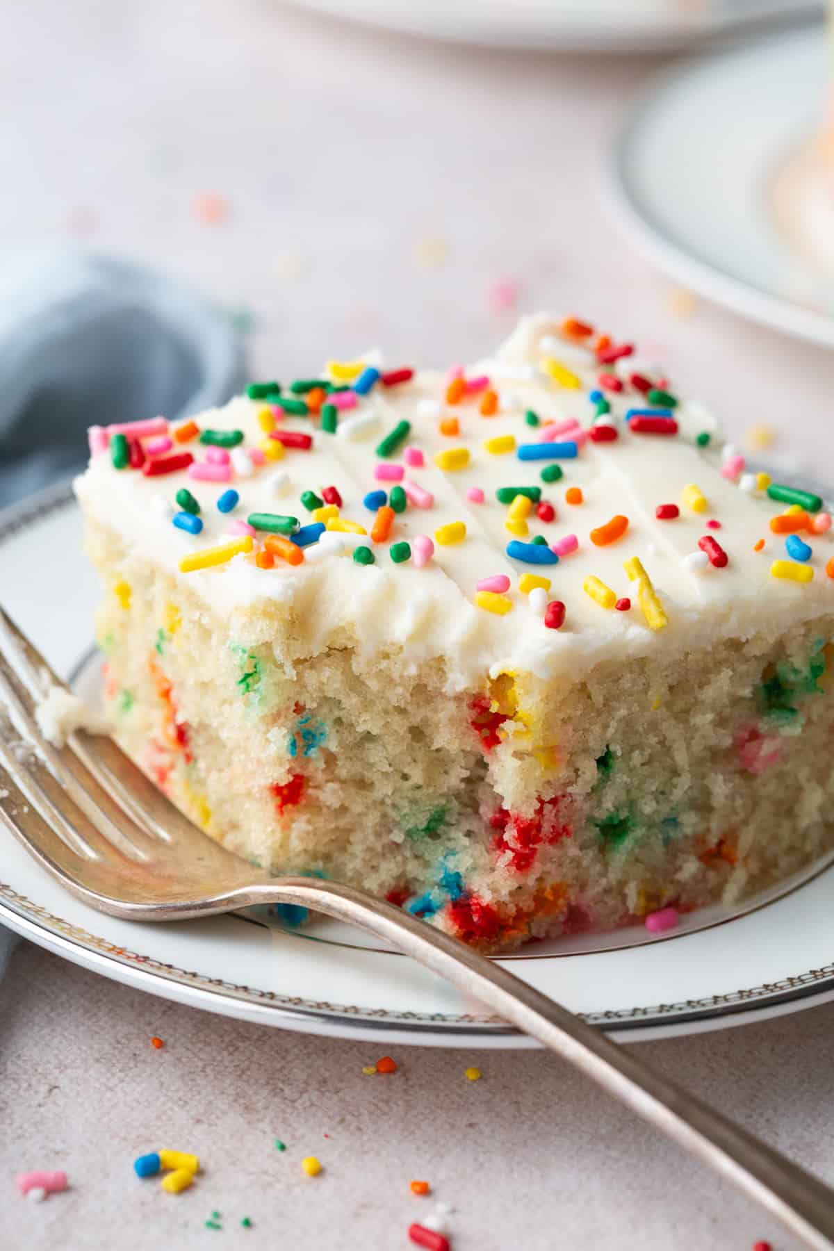 vanilla wacky cake with sprinkles inside and on top, sitting on a white plate with a bite taken out, and a fork in front.