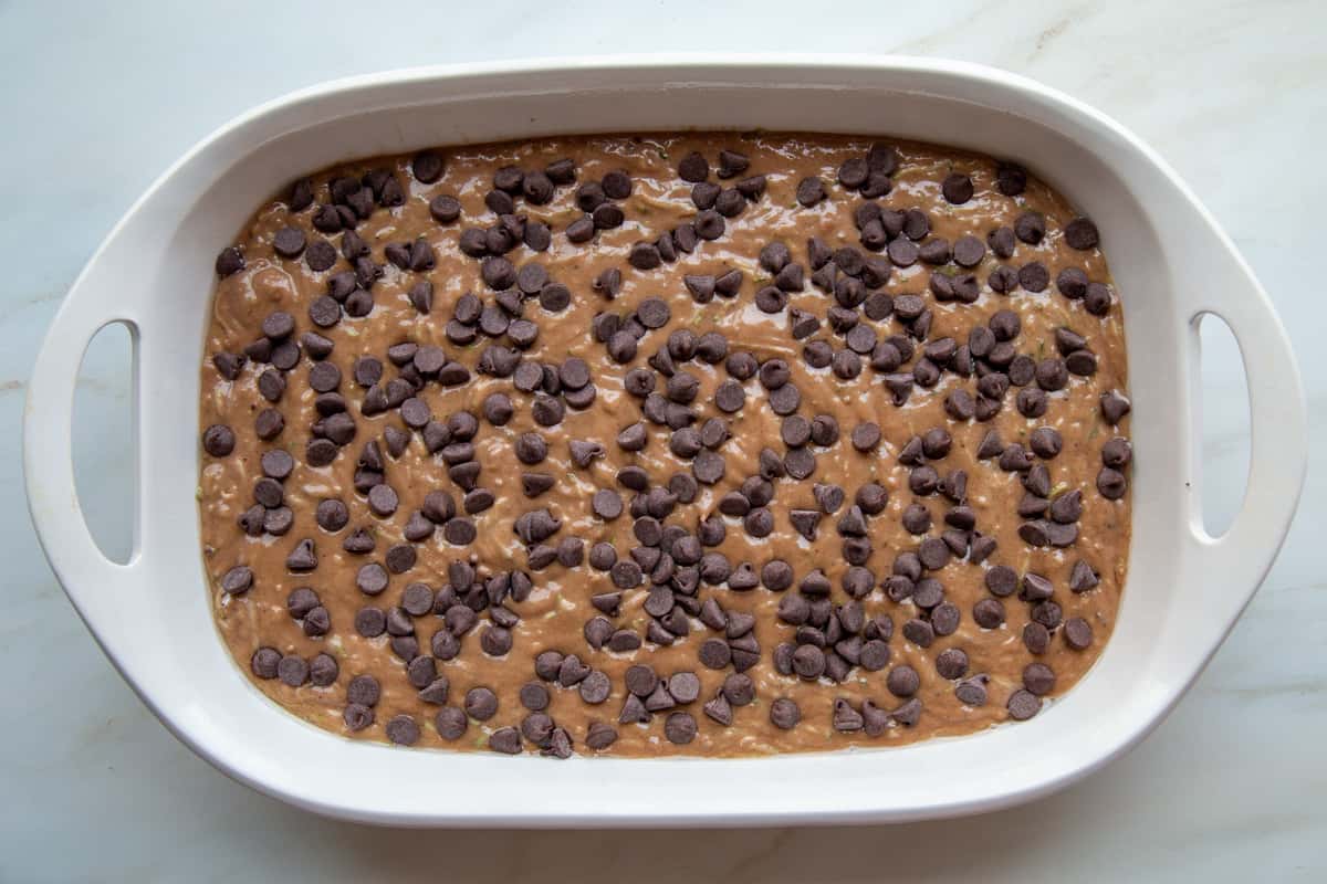 chocolate chips on top of zucchini cake batter in a white baking dish.