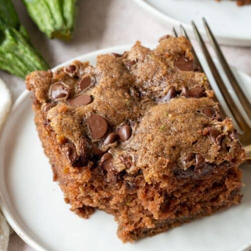 slice of chocolate chip zucchini cake with a bite taken out on a white plate.