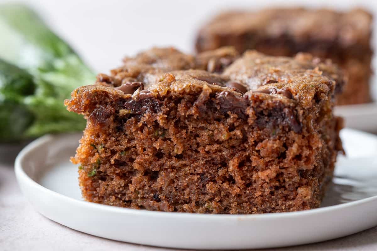 slice of chocolate zucchini cake with chocolate chips on a white plate.