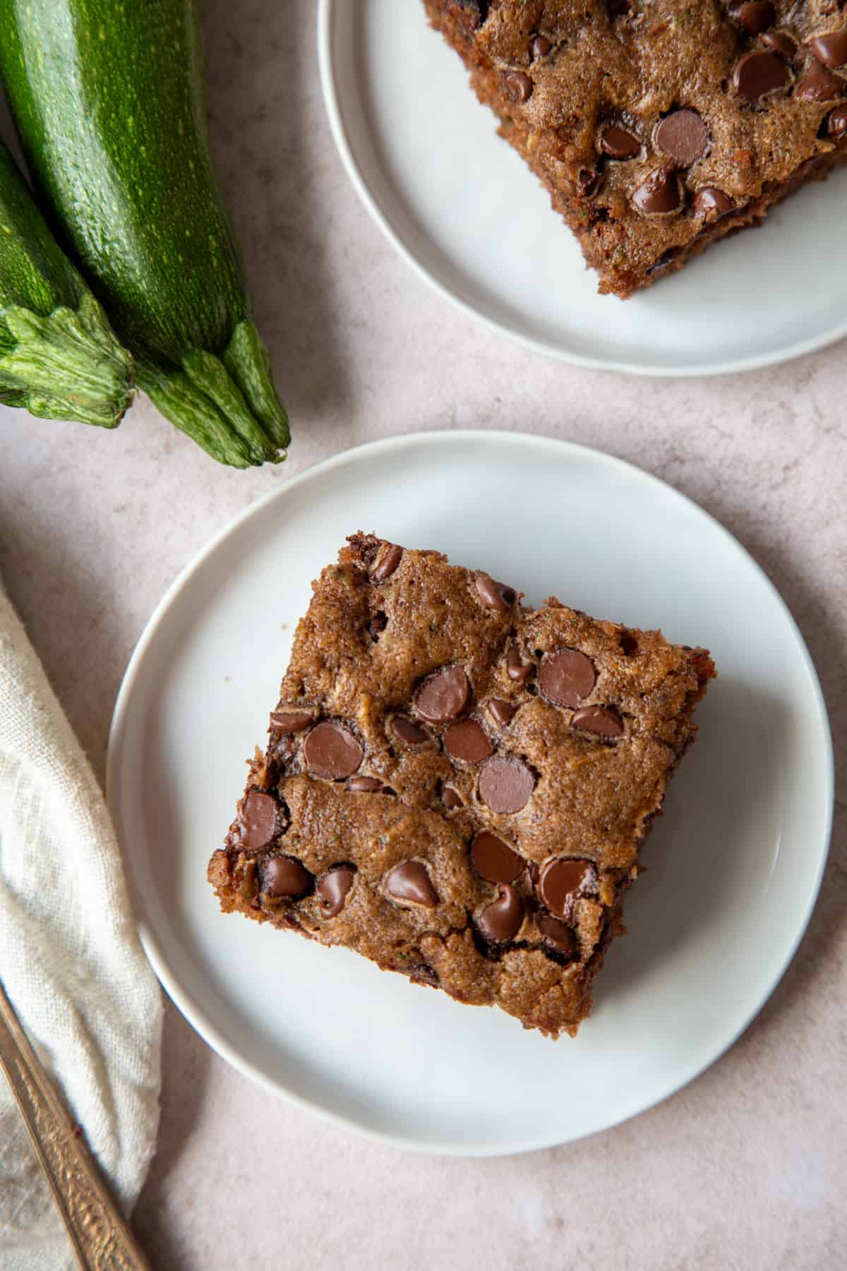 slices of chocolate chip topped zucchini cake on white plates next to whole zucchini.