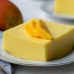 square piece of creamy mango jello salad on a white plate topped with slices of fresh mango.