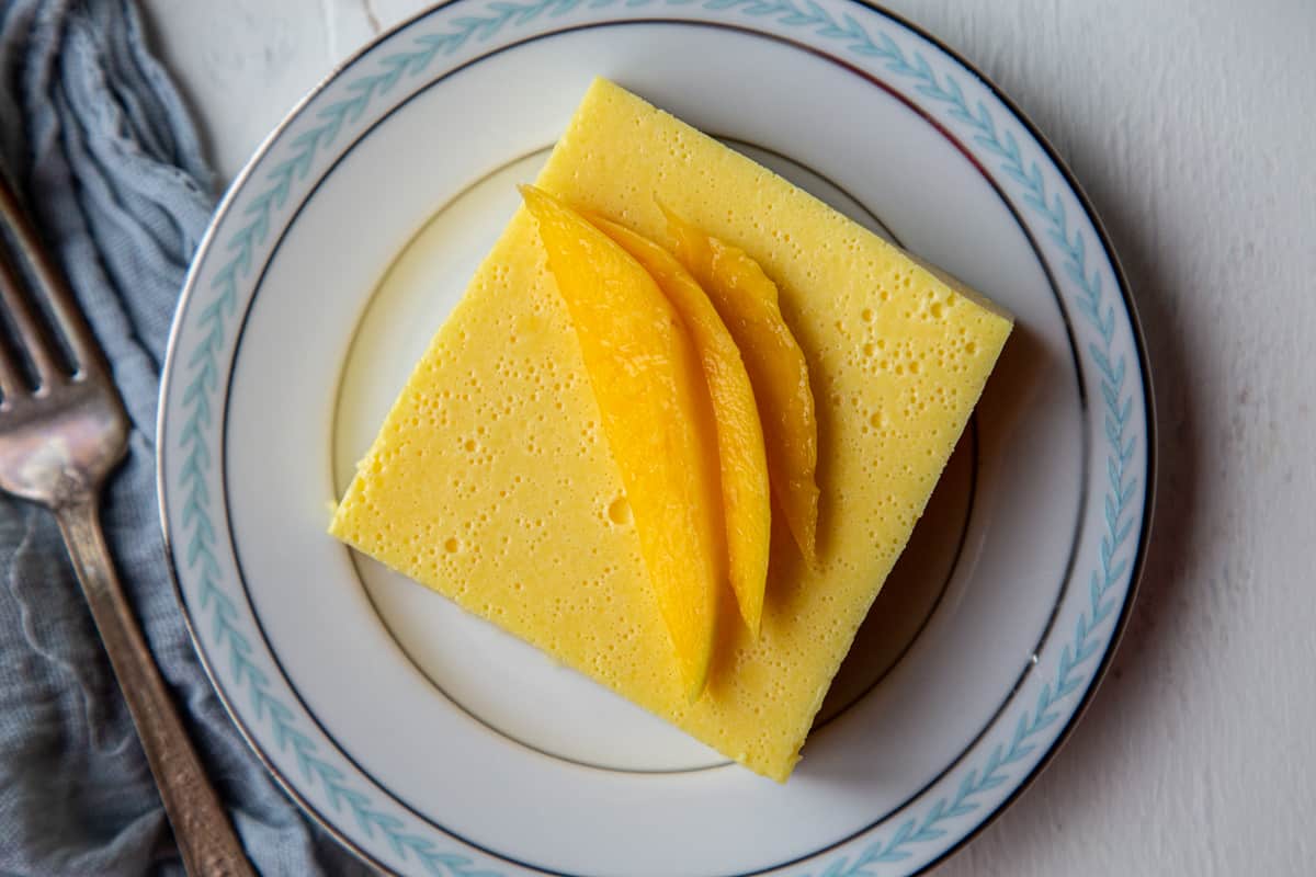 square of creamy mango salad on a white plate with a blue rim, topped with small slices of fresh mango.