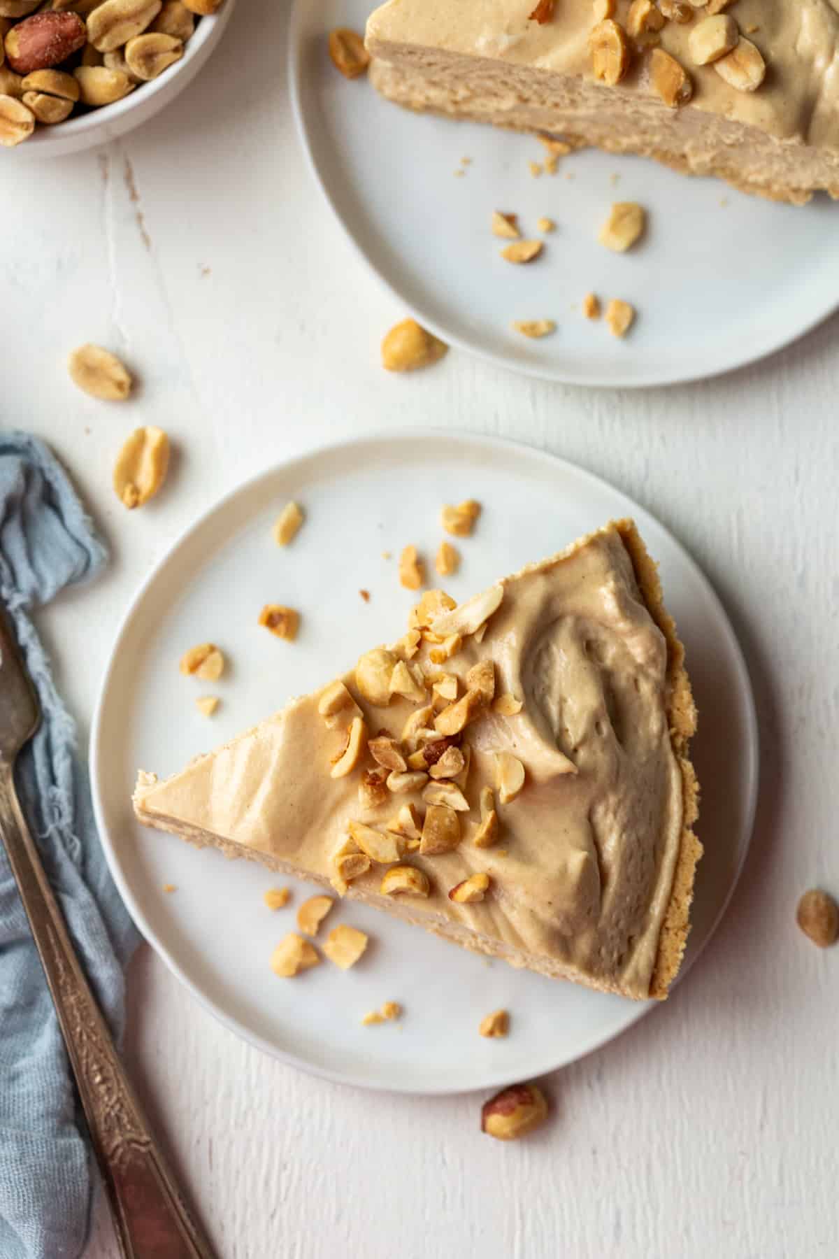 slice of creamy peanut butter pie on a white plate, topped with crushed peanuts.