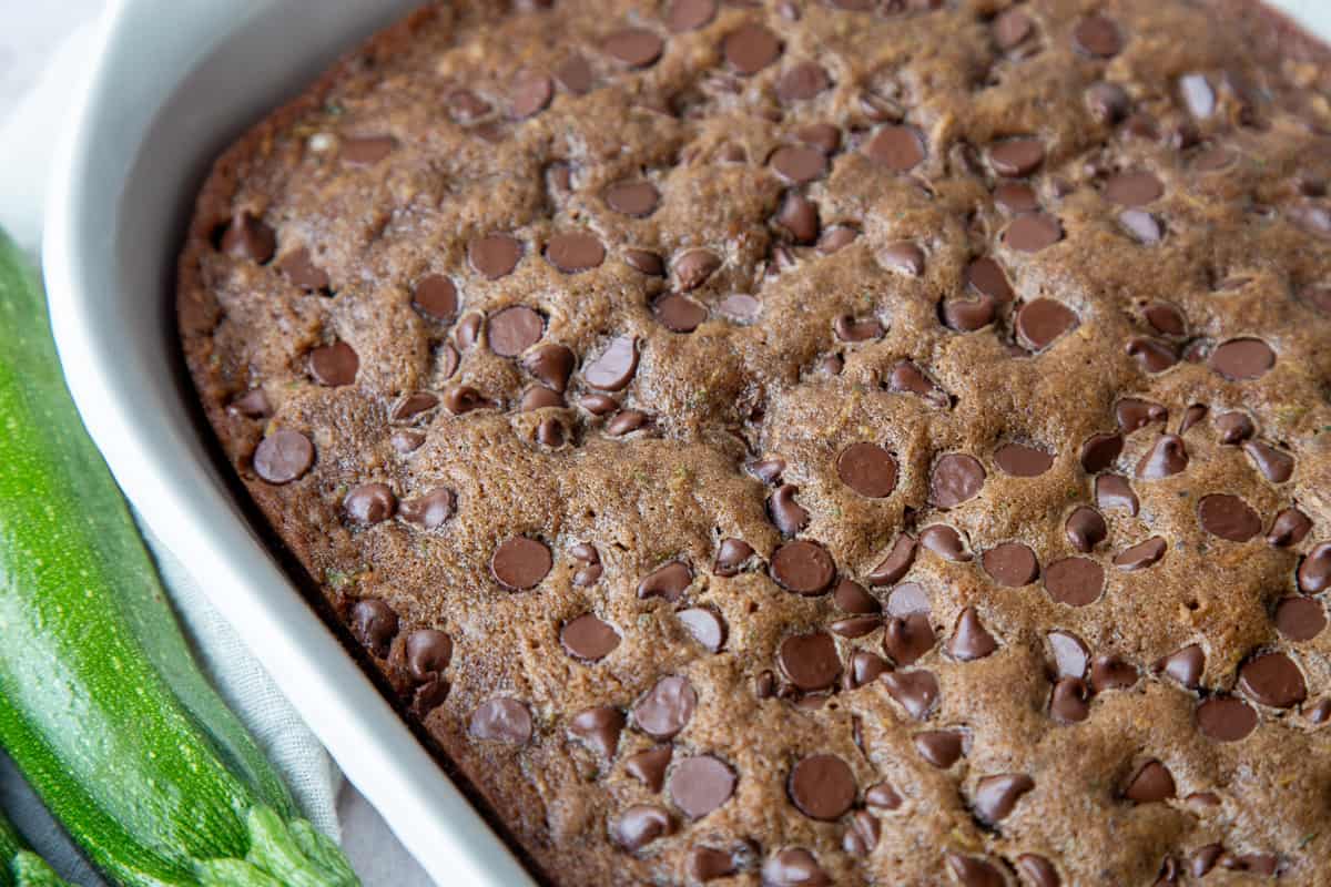 zucchini cake in a white dish topped with chocolate chips.
