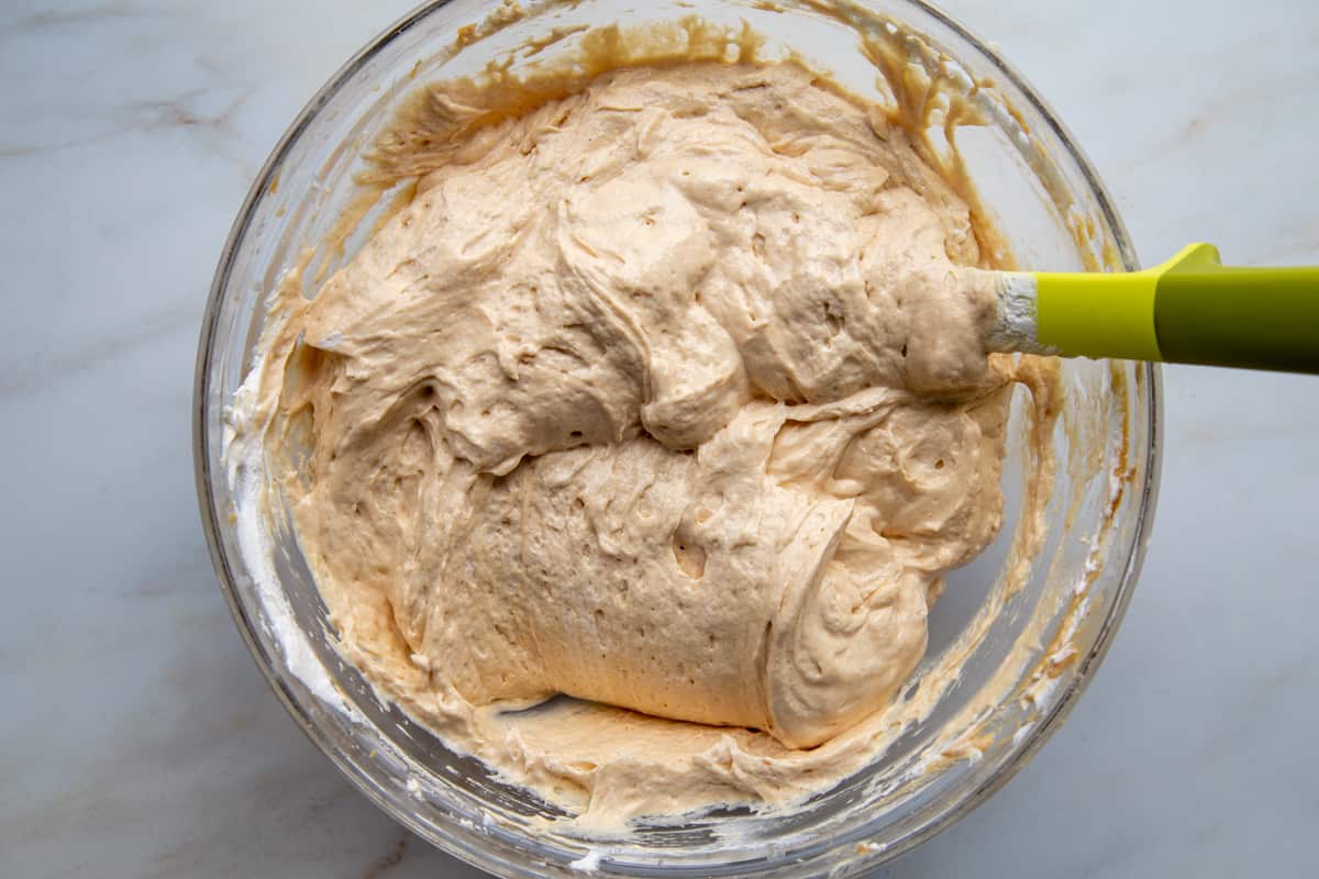 light and fluffy peanut butter mixture in a glass bowl with a yellow and green spatula.