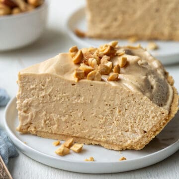 slice of creamy old fashioned peanut butter pie on a white plate, topped with chopped peanuts.