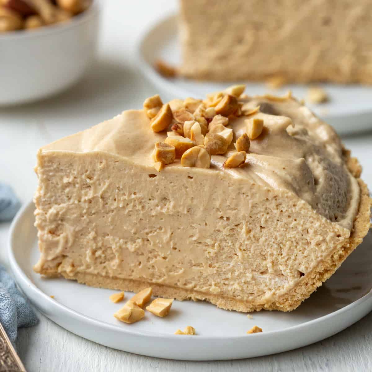 slice of creamy old fashioned peanut butter pie on a white plate, topped with chopped peanuts.