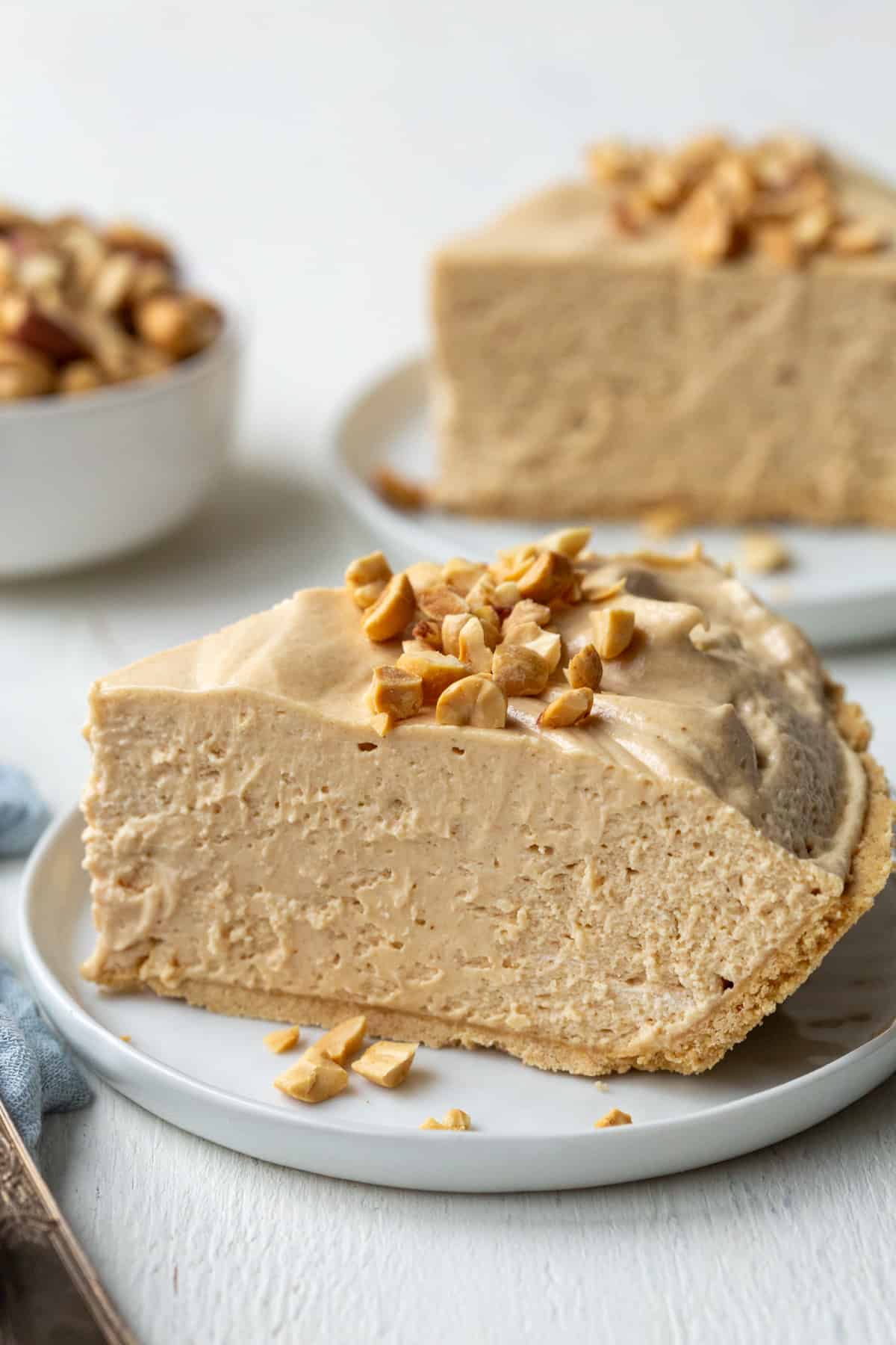 slice of creamy peanut butter pie topped with crushed peanuts on a small white plate.