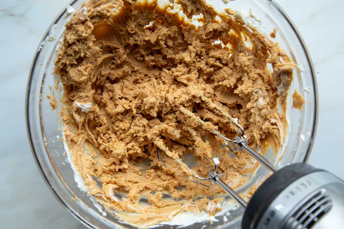 peanut butter cream cheese mixture in a glass bowl with a hand mixer.