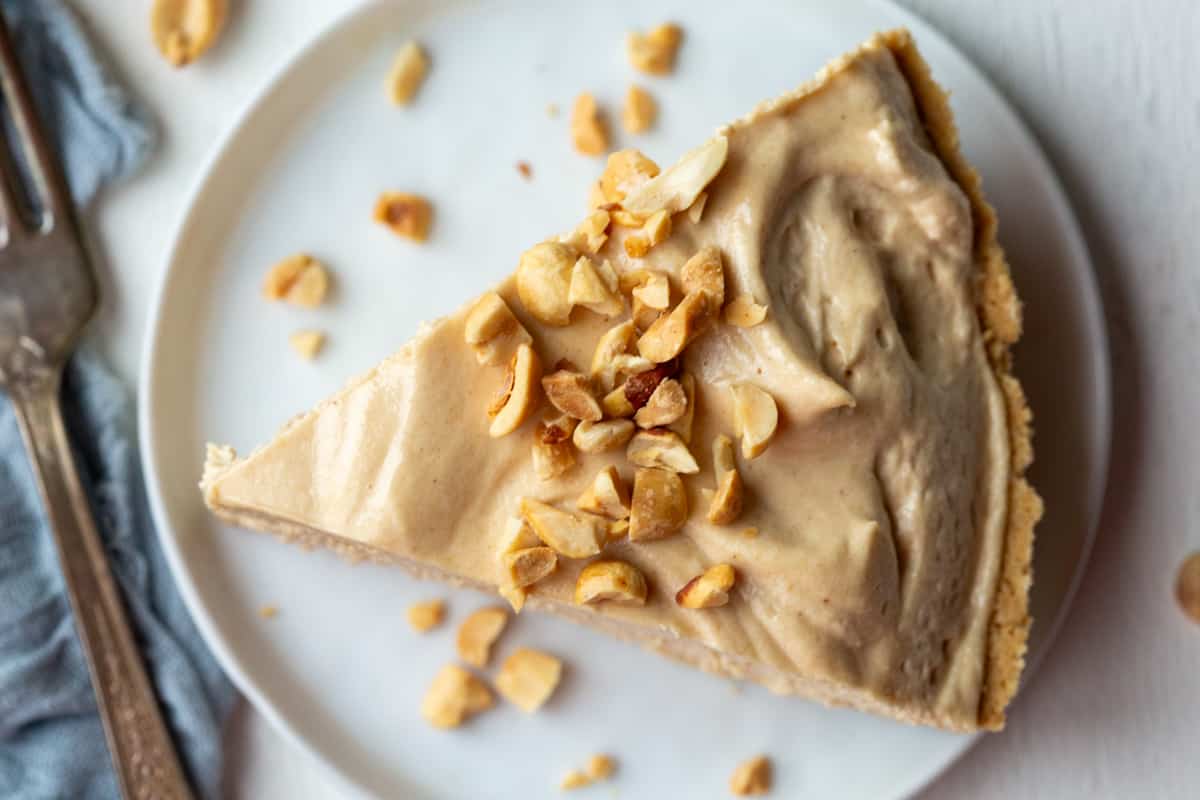 slice of old fashioned peanut butter pie topped with chopped peanuts on a white plate.