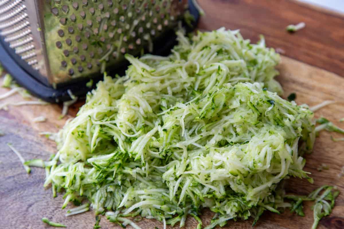 pile of shredded zucchini next to a box grater.
