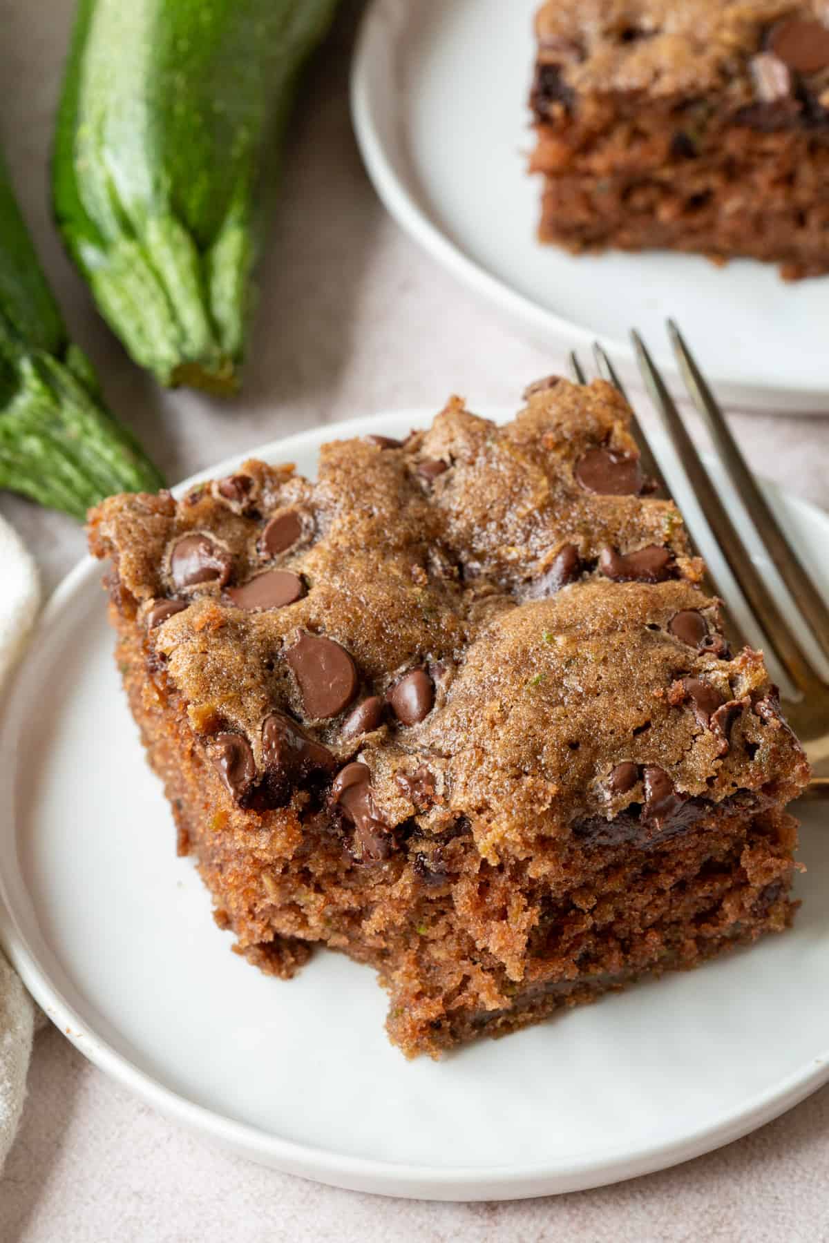 slice of chocolate chip zucchini cake with a bite taken out, next to whole zucchini.