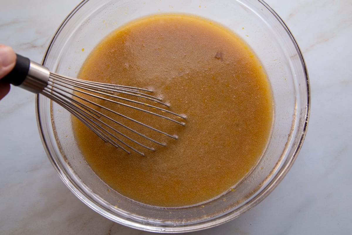 hand whisking a sugar and butter mixture in a glass bowl.