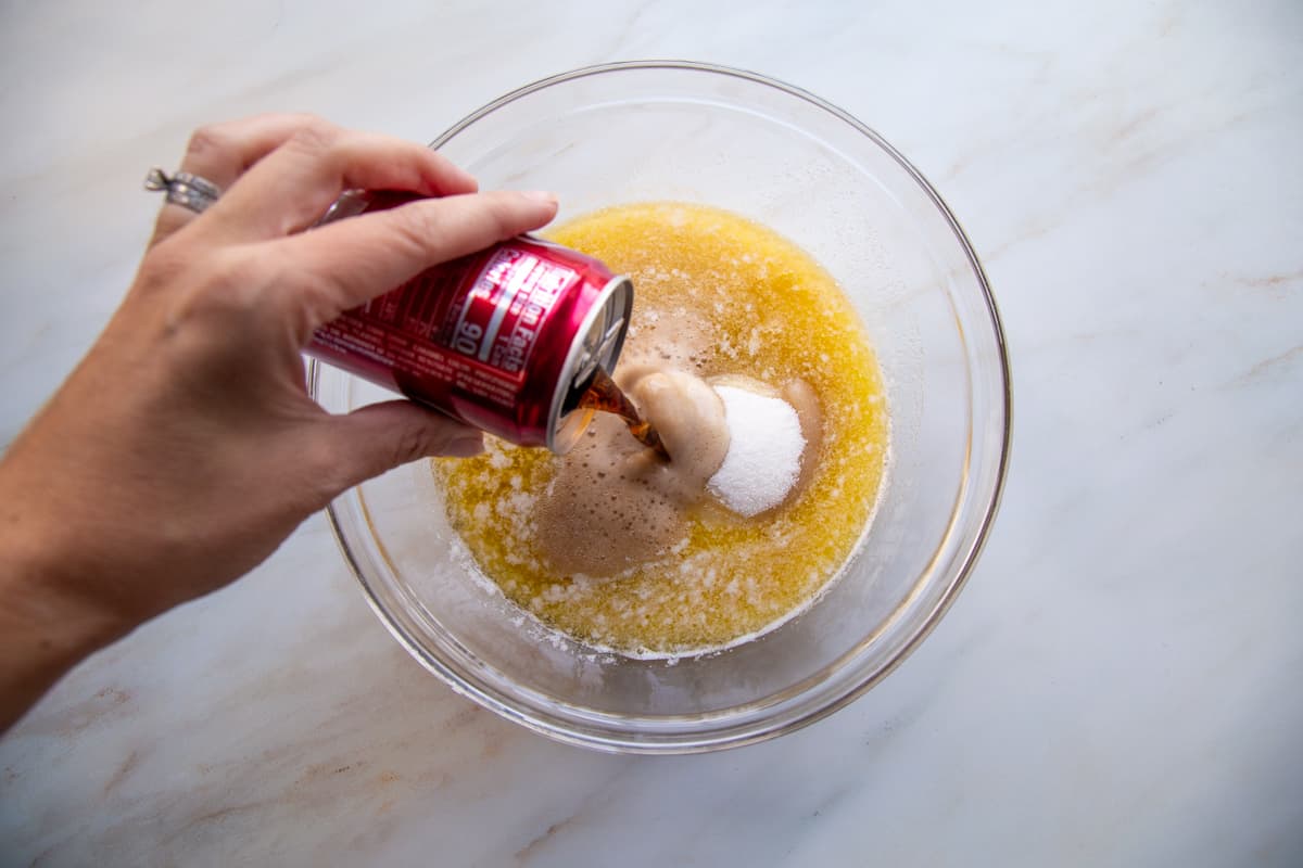 hand pouring dr. pepper into a bowl with butter and sugar.