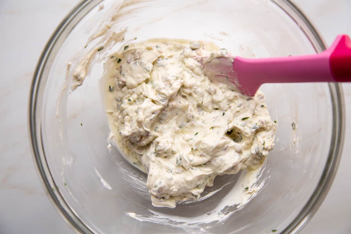 cream cheese mixture in a glass bowl with a pink spatula.
