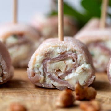 ham rollups with cream cheese secured with toothpicks on a wooden serving board.