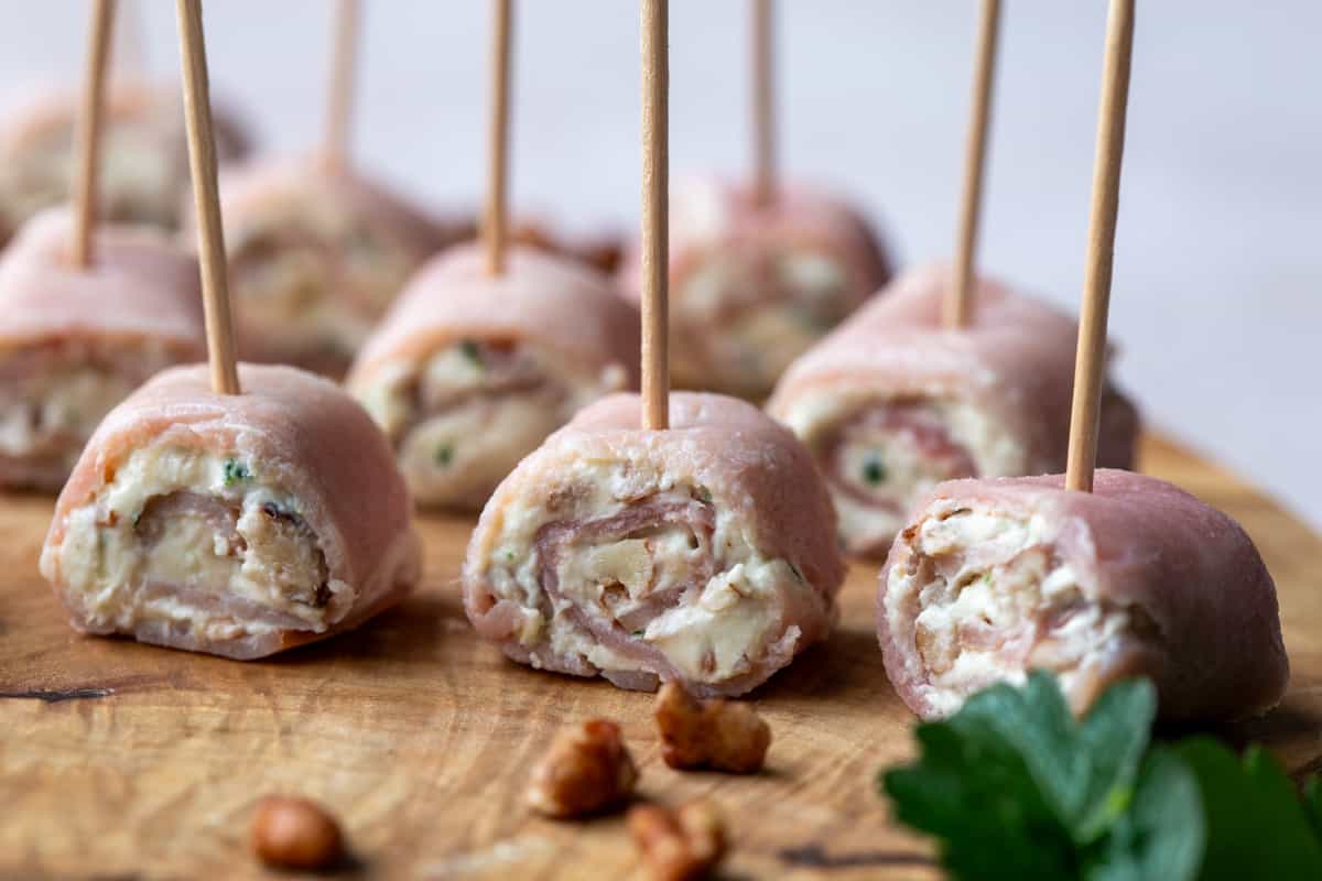 ham and cream cheese pinwheels secured with toothpicks on a wooden board.