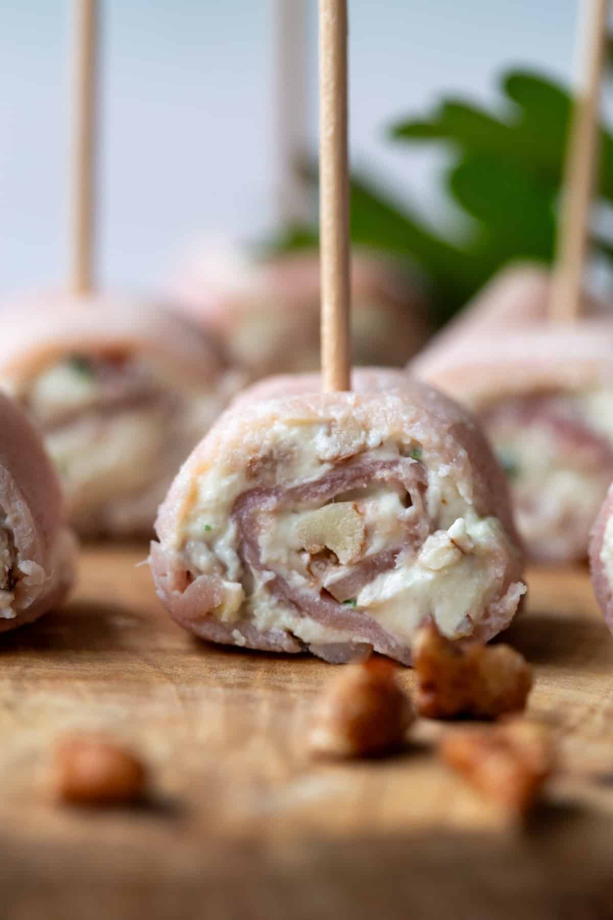 ham pinwheel stuffed with cream cheese on a wooden board, secured with a toothpick.