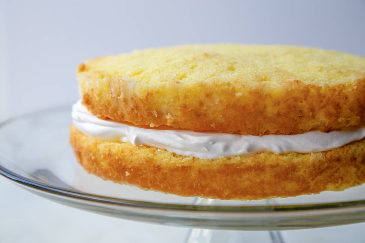 two cake layers with cool whip in between on a glass cake stand.