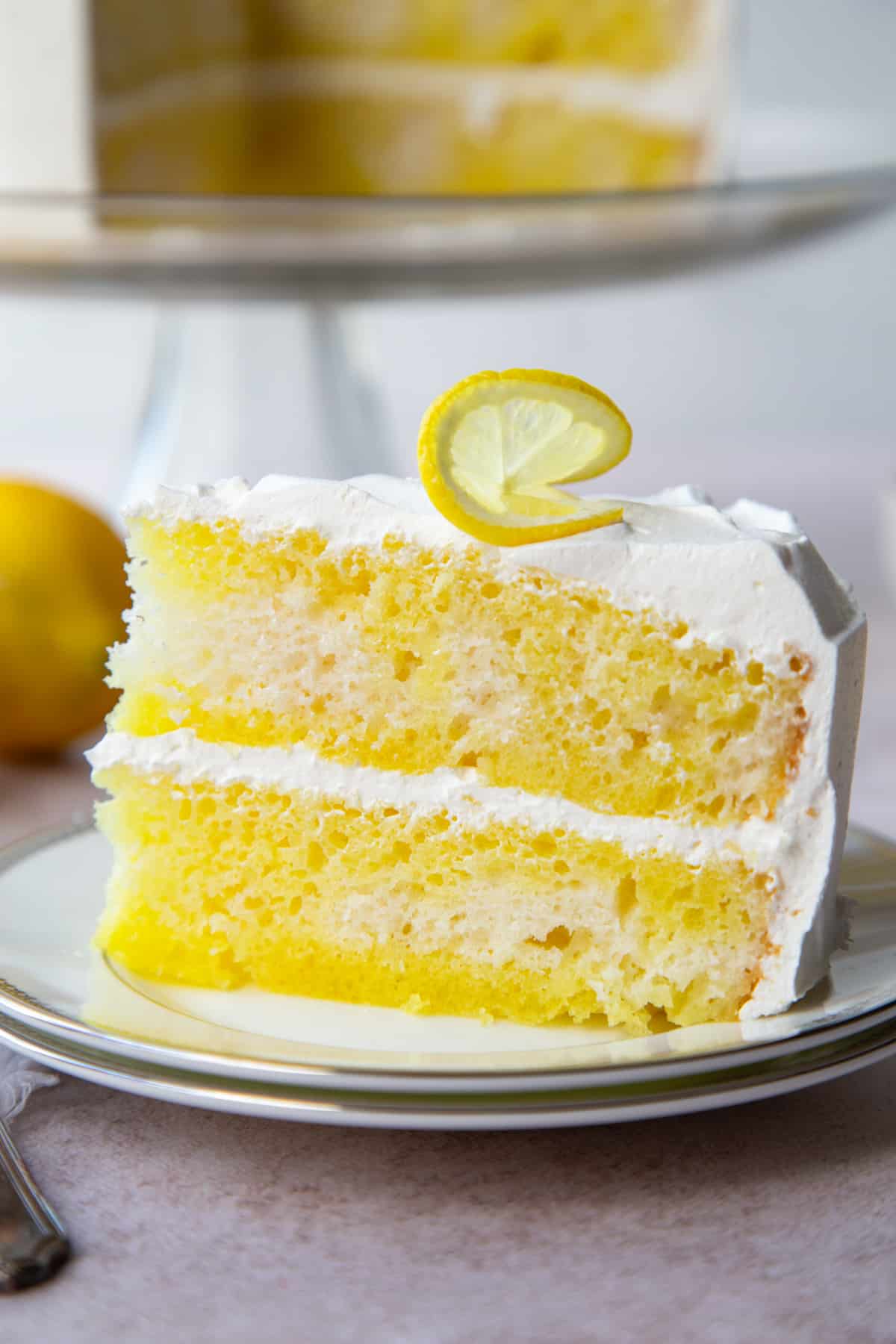 slice of lemon poke cake with a whole cake in the background.