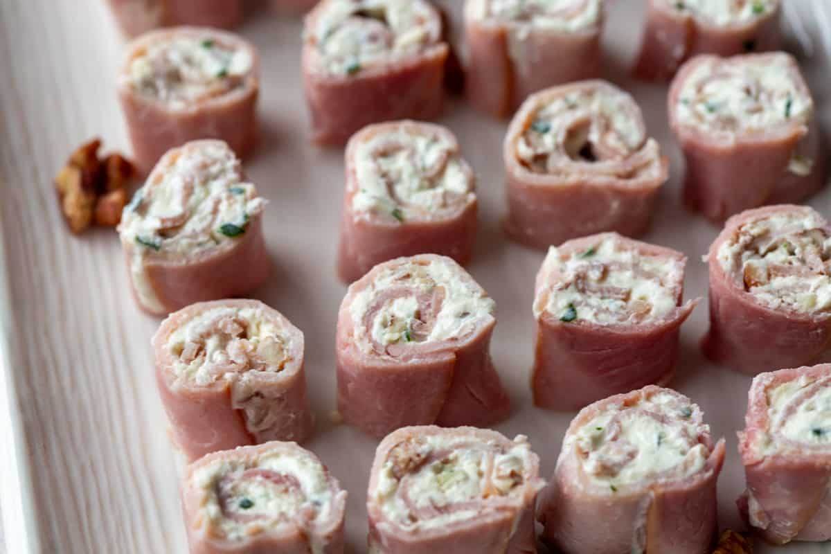 ham pinwheels with cream cheese lined up on a white platter.