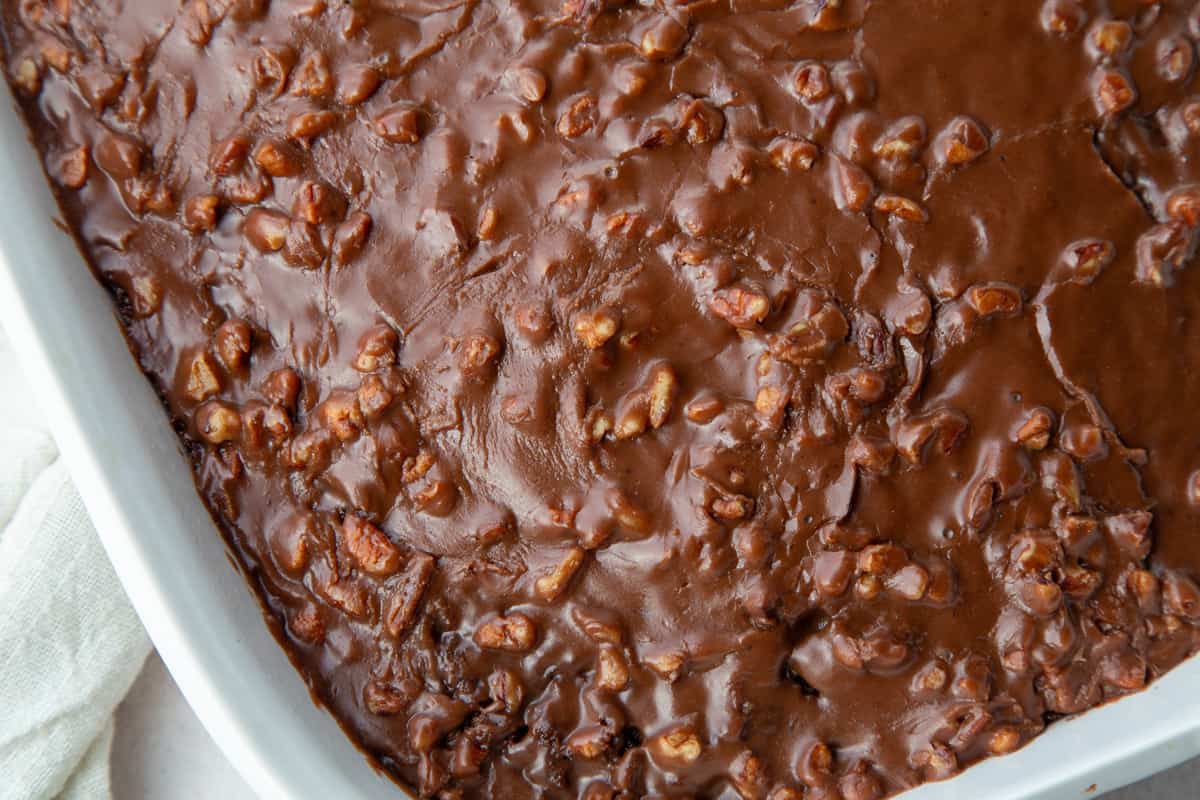 dr. pepper cake in a white casserole dish, topped with chocolate pecan frosting. 