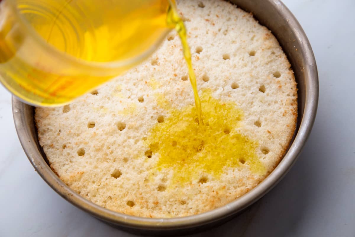 lemon gelatin being poured over a cake with holes in it.