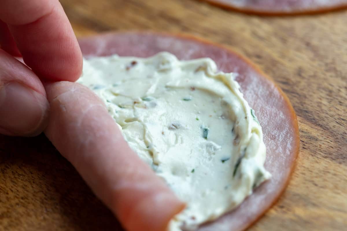 hand rolling a slice of ham covered with cream cheese into a log.