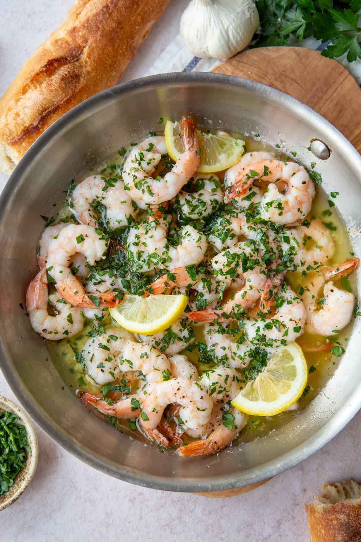 shrimp scampi with lemon slices in a skillet surrounded by hunks of baguette.