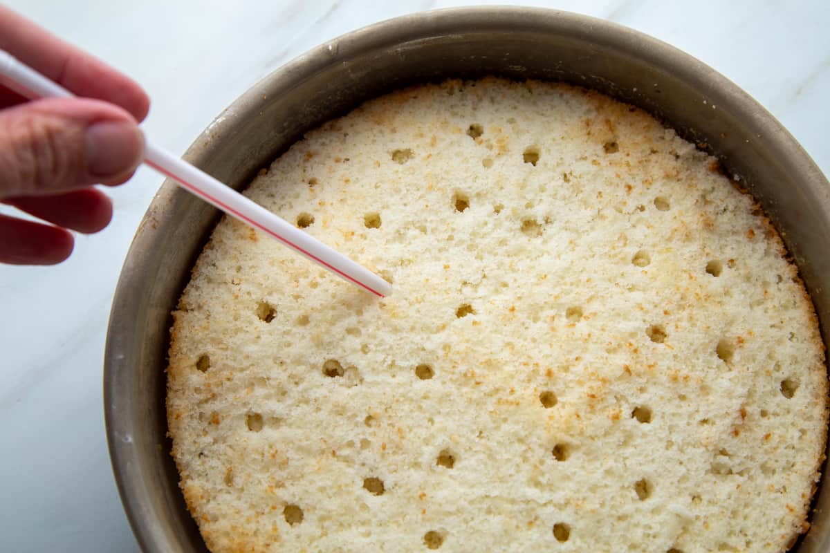 hand holding a straw poking holes in a cake.