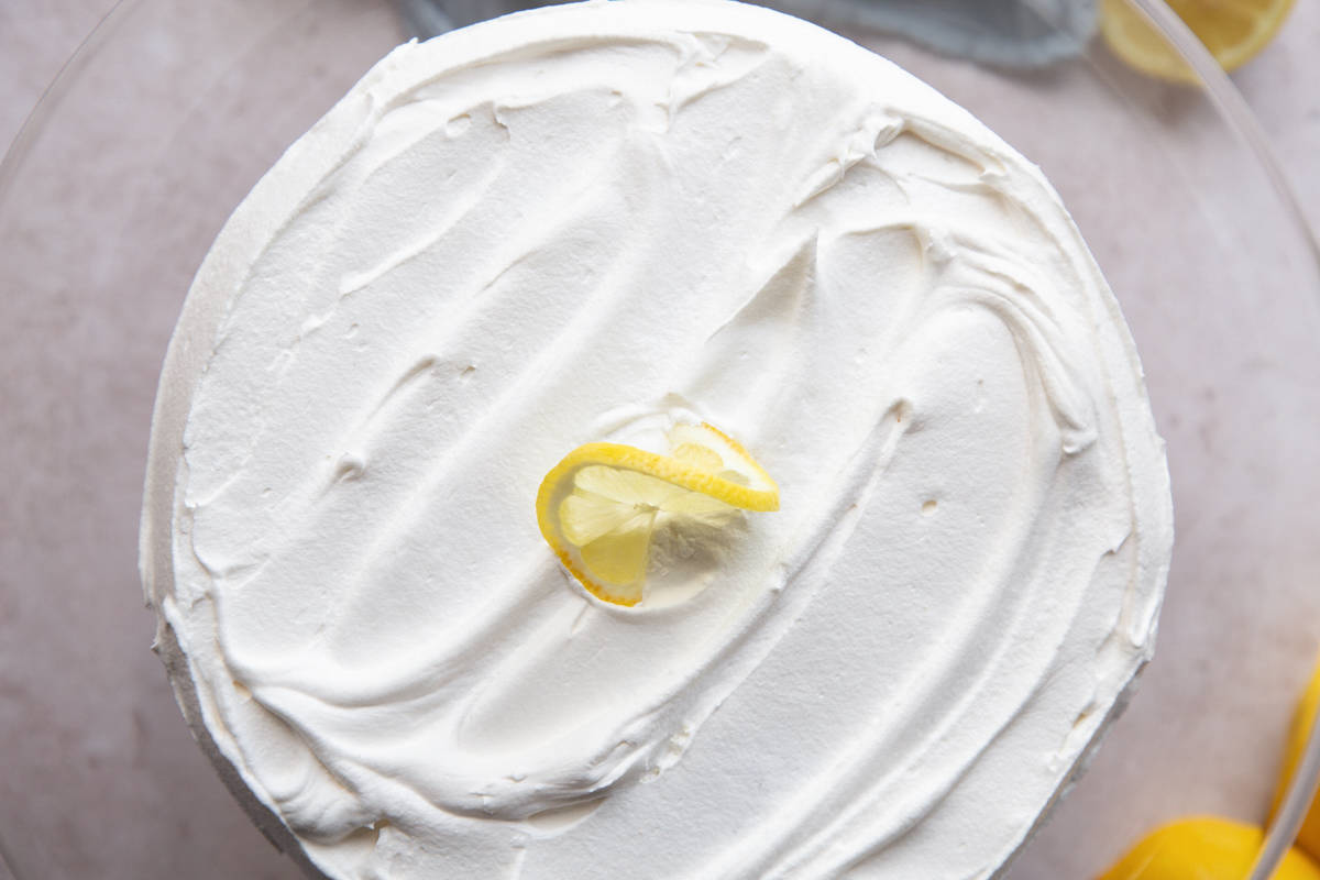 lemon poke cake covered in cool whip and garnished with a lemon twist.