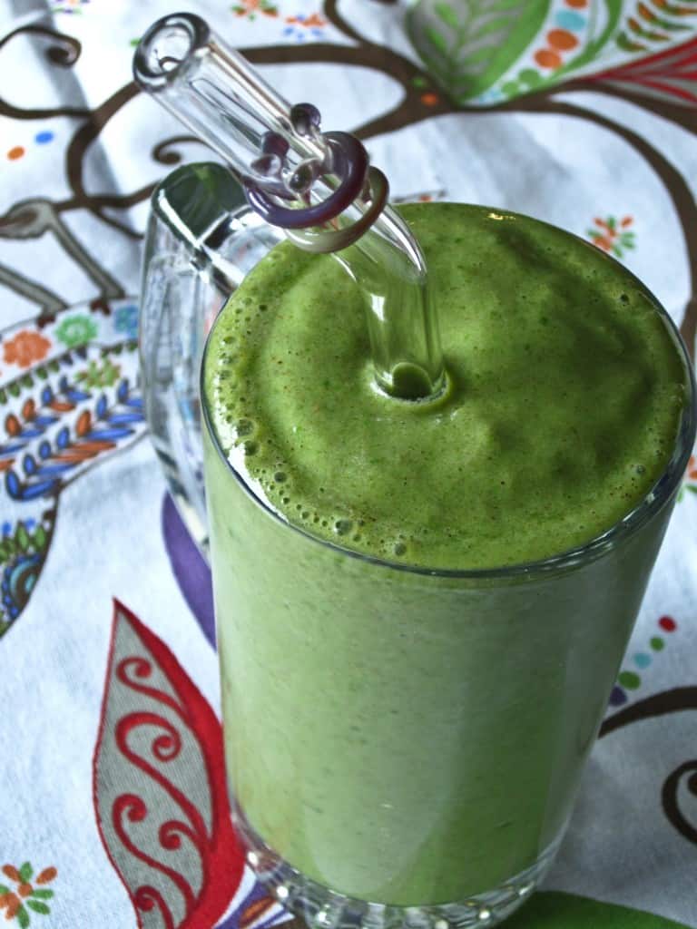 Top view of an Almond Pear Green Smoothie in a tall glass cup with a fun straw in it.