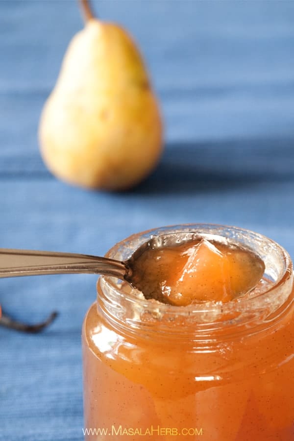 Close up of a spoonful of Vanilla Pear Preserves on a silver spoon inside the rim of a mason jar.