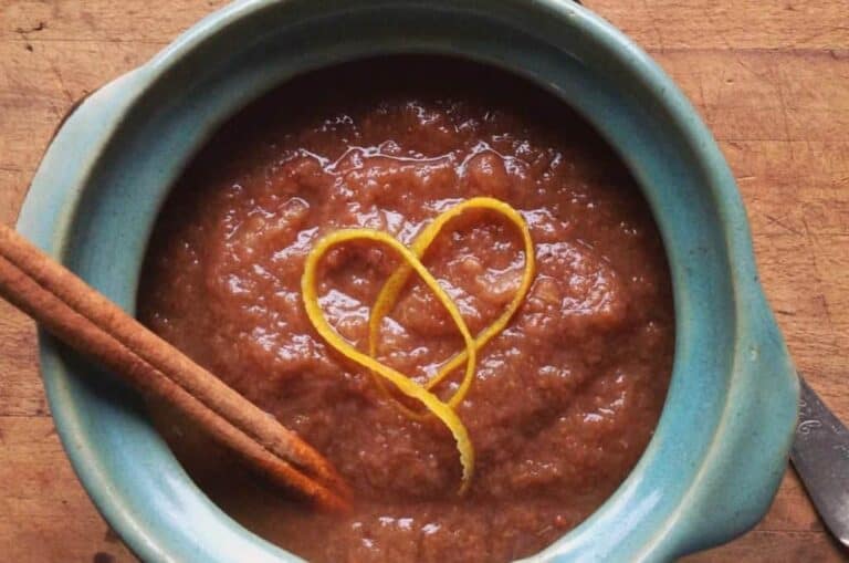 Top view of Spice Pear Sauce in a light blue slow cooker with orange peels and a cinnamon stick.