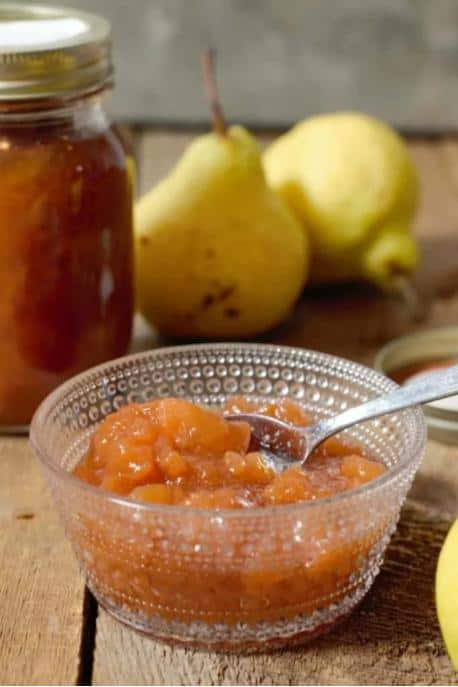 Small glass bowl of Homemade Pear Preserves on a wooden surface with pears in the background.