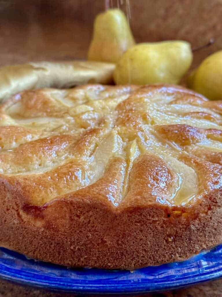 Side view of a freshly baked Honey Pear Cake on a blue plate with pears in the background.