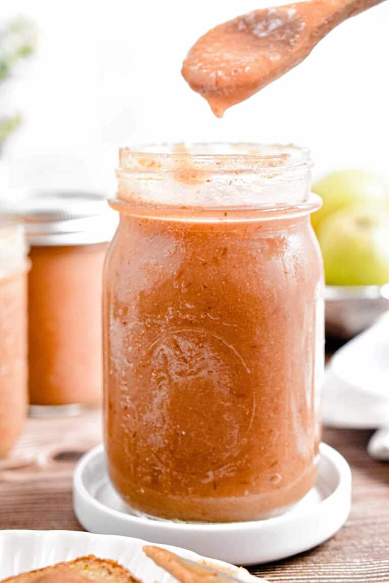 A wooden spoon lifting some Instant Pot Pear Butter from a mason jar sitting on a small white plate.