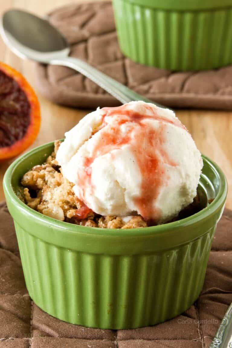 Pear Crisp in a small green ramekin with a scoop of vanilla ice cream topped with Blood Orange Sauce.