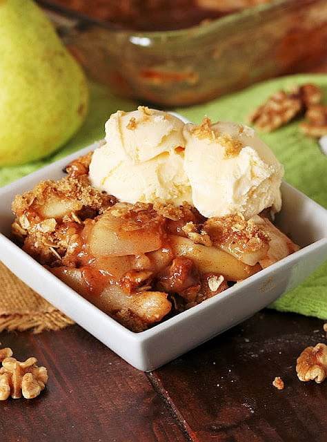 Small square bowl of Pear Walnut Crisp with two scoops of ice cream on top.